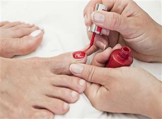 Manicurist Applying Red Nail Polish On Customer