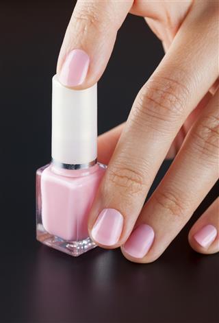 Pink bottle of nail polish in woman hand