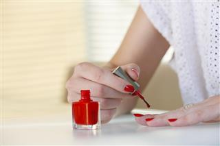 Woman applying red nail polish on her fingers