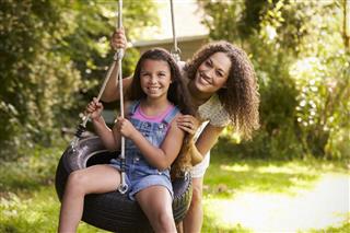 Mother Pushing Daughter On Tire Swing