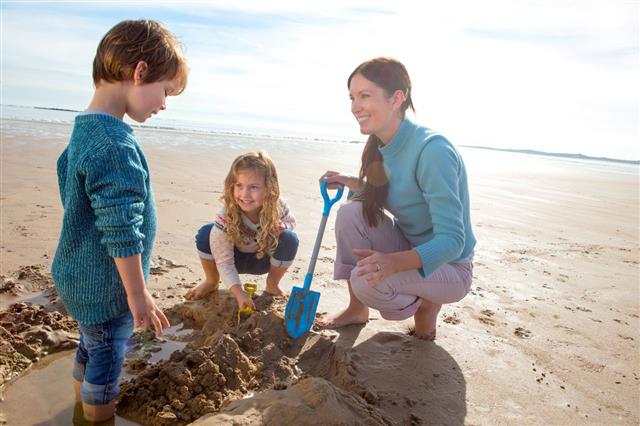 Mother And Children Digging On Beach