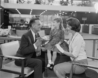 Girl sitting on table with parents beside her