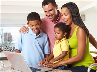 Happy family of four using laptop in kitchen together