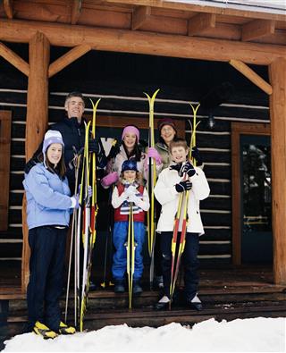 Parent and children holding cross-country skis on porch