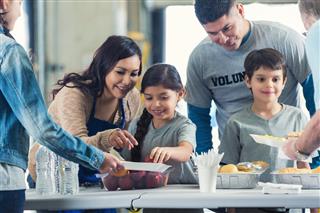Family serving meals while they volunteer in soup kitchen together