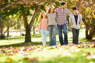 Family of four walking in autumn leaves at park