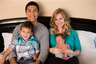 Happy Mixed-Race Family Sitting on Bed Together