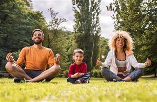 Young happy family doing Yoga relaxation exercises on a grass