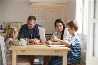 Parent Helping Children With Homework At Kitchen Table
