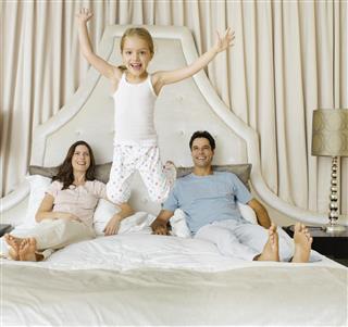 A young girl jumping on a bed her parents are lying in