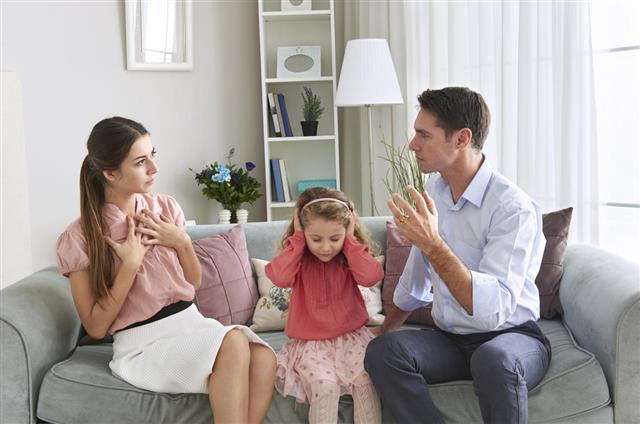 Girl covering ears with hands while her parent arguing