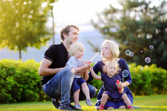 Young family with their toddler children blowing soap bubbles