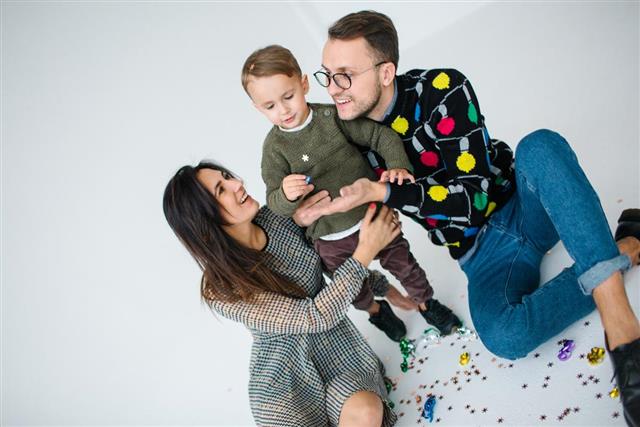 Young couple with son celebrating with confetti over white background