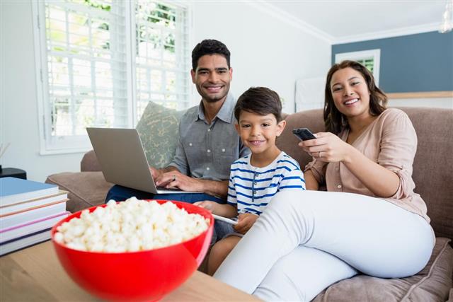 Mother watching television while father and son using laptop at home