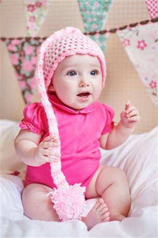Newborn Baby Girl In Pink Knitted Hat On The Bed