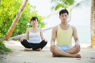 Chinese Man and Woman performing yoga on tropical beach