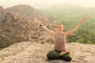 Woman practicing yoga at mountain cliff on sunrise