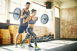 Woman lifting barbell while personal trainer assisting her in gym