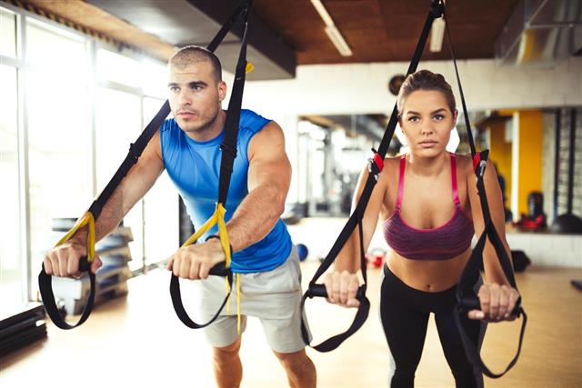 Couple doing arm exercises with suspension straps at gym