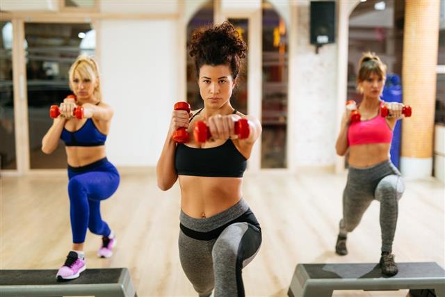 Women exercising step aerobics with dumbbells at the gym