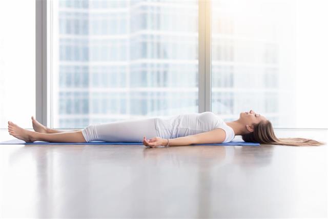 Young attractive woman in Corpse pose against floor window