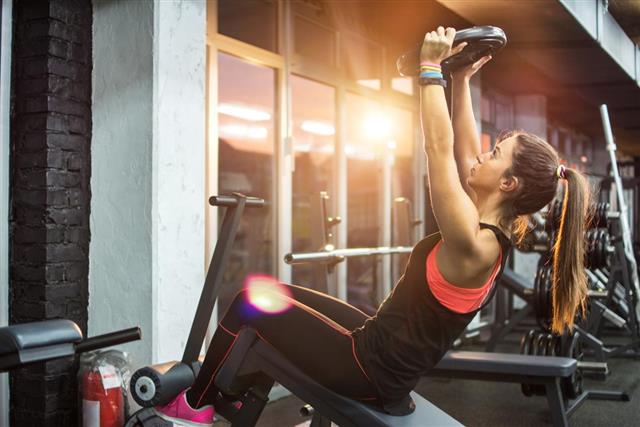 Sporty woman holding up weight plate while exercising gym machine