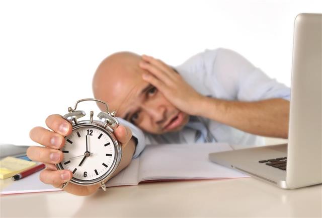 Overworked exhausted bald business man with computer and alarm clock