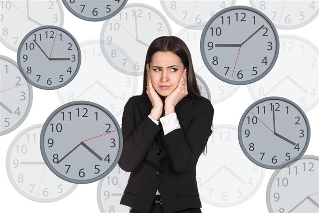 Businesswoman stands among clocks