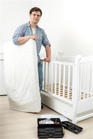 Smiling man standing with mattress at disassembled baby's cot