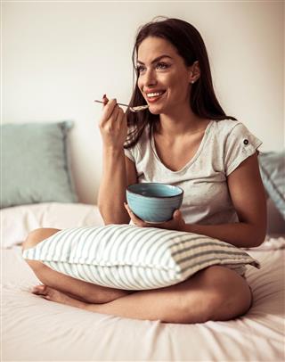 Smiling woman in the morning eating breakfast in bed.