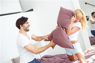 Young playful couple enjoying pillow fight.