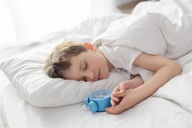 Little boy sleeping in white bed with alarm clock