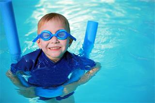 Child With Noodle Float And Swimming Goggles Learning To Swim