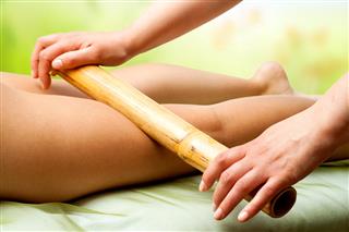 Hands Massaging Female Legs With Bamboo