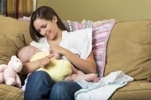 Young mother breastfeeding her baby daughter at home