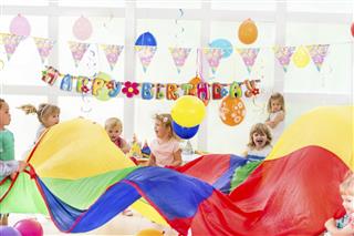 Cheerful children playing with parachute on birthday party.