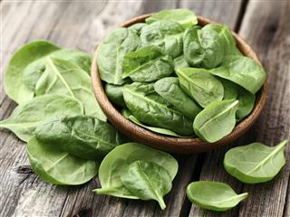 Fresh baby spinach leaves in a bowl on a wooden table