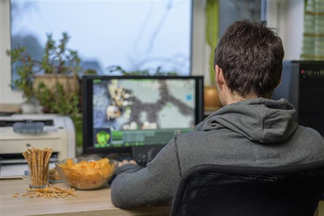Male gamer playing strategy game on computer eating snacks