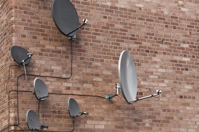 Many satellite dishes on a brick wall
