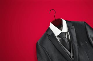 Mens dark grey suit on clothes hanger on red background.