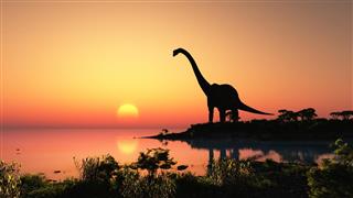 Silhouette of dinosaur at a lake at sunset