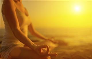 Hand of woman meditating in yoga pose at sunset