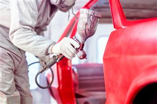 Professional worker spraying red paint on a car body