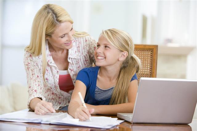 Woman helping young girl do homework in dining room
