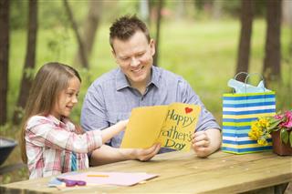 Daughter shows dad handmade Father's Day card. Outdoors. Child parent