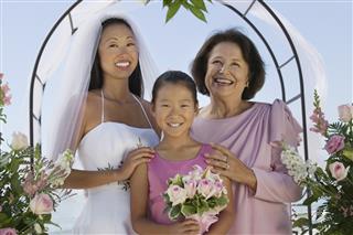 Bride With Mother And Flower Girl Standing Against Sky