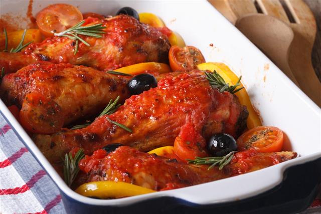 Chicken legs baked in tomato with olives closeup.