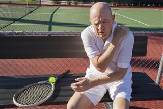 Senior male tennis player shoulder pain sitting at court