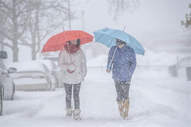 Two teenager girls with umbrellas under snowfall at the street