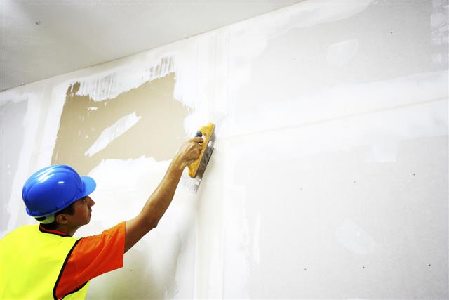 Decorator wearing blue hat and yellow jacket plastering wall